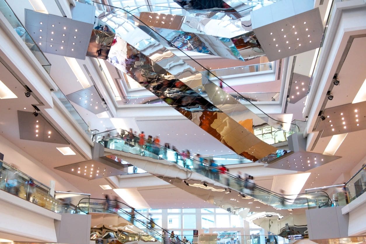 A mall with many people on escalators and glass windows.